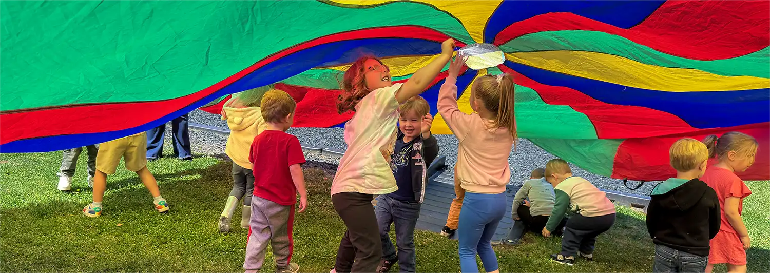 Children playing together under a colorful parachute at the Sybene site.