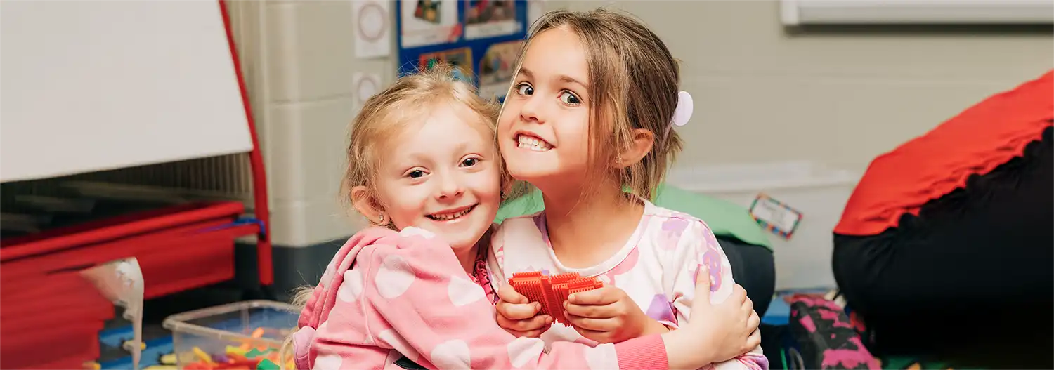 Two children hugging and smiling in a Symmes Valley classroom.