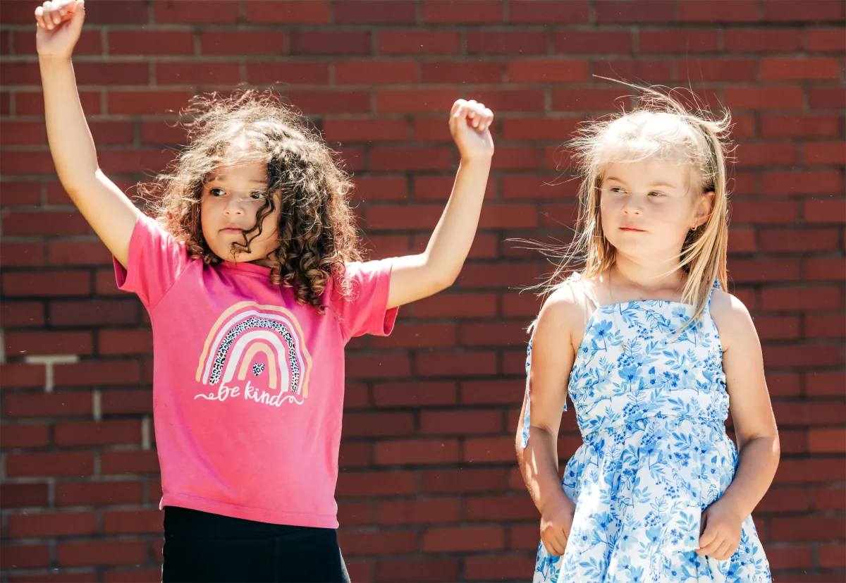 Two young children playing outdoors on a sunny day beside a brick school wall.