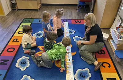 Children and a teacher gathered on the alphabet rug for morning circle