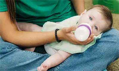 A caregiver bottle-feeding an infant